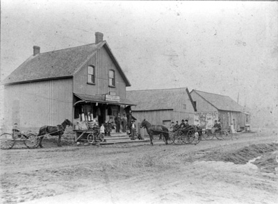 Reproduction d’une photographie d’un magasin g&eacute;n&eacute;ral, moulin pour la pr&eacute;paration de moul&eacute;e et fromagerie, au coin de McCrimmon, Alexandria (Ontario), 1900.